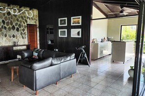 A modern living area with a black leather sofa, a telescope, and framed pictures on the wall. - Hypnosis Haus - Secluded Oceanview Villa—5-Minutes to Beach (Grenadines)