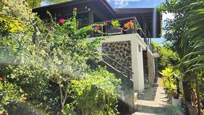 A modern building with a stone facade, a balcony with potted plants, and a staircase leading to the entrance.