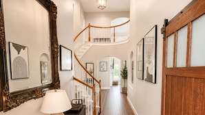 A hallway with a wooden floor, a staircase with white railings, a large mirror, and framed artwork on the walls. - Lakefront Oasis w/covered Patio + outdoor Kitchen (Fort Worth)