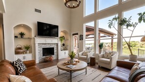 A spacious living room with a fireplace, leather sofas, a coffee table, and large windows offering a view of the outdoors. - Lakefront Oasis w/covered Patio + outdoor Kitchen (Fort Worth)