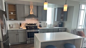 Cocina moderna con armarios grises, electrodomésticos de acero inoxidable y una isla central con taburetes.