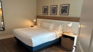 Una habitación de hotel con cama, mesitas de noche, piso de madera y tres cuadros en la pared.