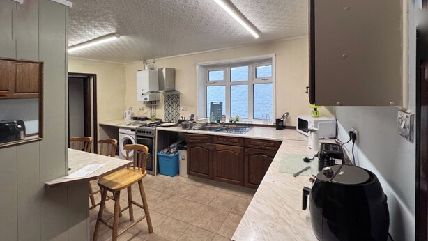 A kitchen with wooden cabinets, a built-in oven, a window, and a coffee maker. - Affordable & Cozy Seaside Guest House| Cleethorpes (Cleethorpes-Alpine Guest House)