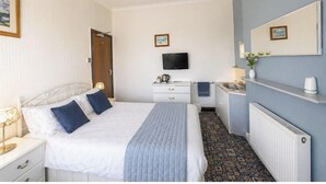 Ein Hotelzimmer mit Bett, Nachttisch, Fernseher, Kommode und einem Badezimmer mit Waschbecken und Spiegel.
