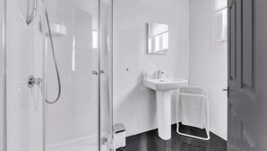 Une salle de bain avec une douche à parois de verre, un lavabo blanc et un porte-serviettes.