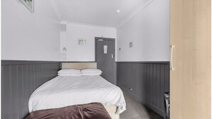 Une chambre à coucher avec un lit, une porte en bois, un mur blanc et un banc marron.