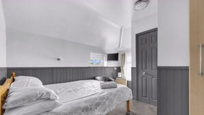 Quarto com cama, uma cadeira, uma televisão e uma porta.