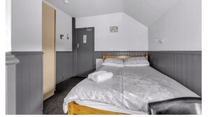 Un dormitorio con cama, una puerta, un interruptor de luz y un pequeño adorno en la pared.