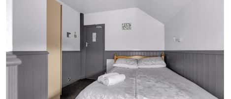 A bedroom with a bed, a door, a light switch, and a small wall decoration.