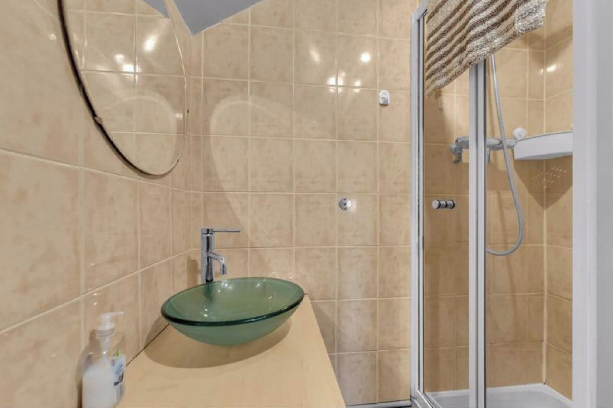 Une salle de bain avec un lavabo en verre, un miroir et un espace douche.