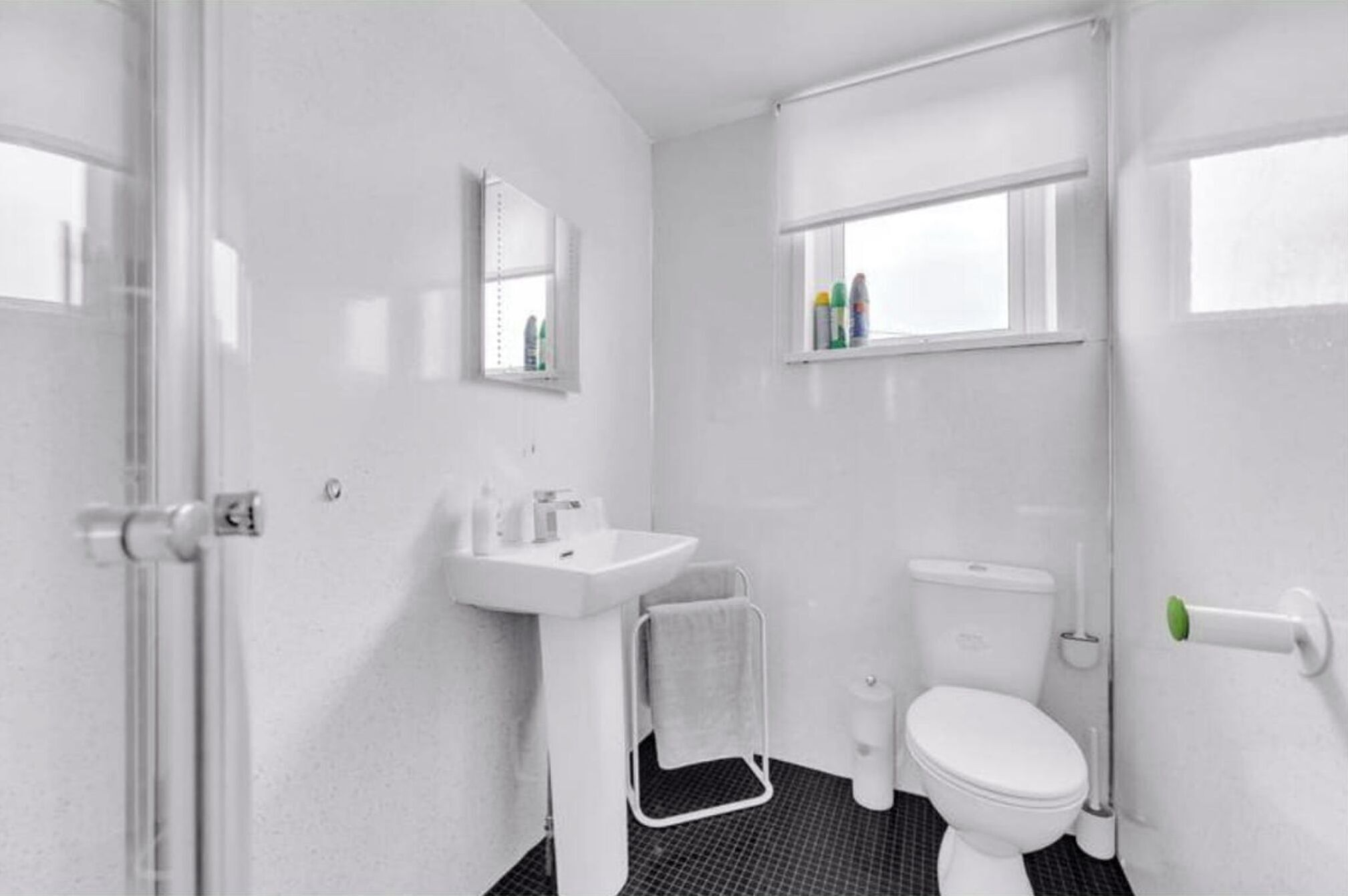Et badeværelse med en hvid vask, toilet og et vindue over toilettet.