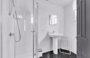Un bagno con cabina doccia in vetro, un lavandino bianco, un porta asciugamani e un cestino.
