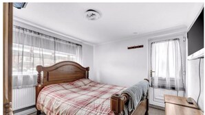 A bedroom with a wooden bed, a bedside table, a window with sheer curtains, and a door with a coat rack. - Mallow View Guest House | Cleethorpes Beachside (Cleethorpes-Mallow View Guest House)