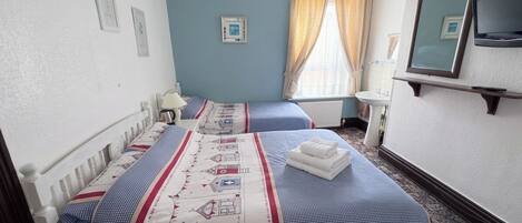 A hotel room with two beds, a television, a window with curtains, and a radiator.