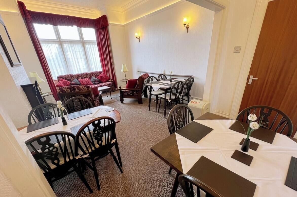 A dining area with a table set for four, a sofa, and a window with curtains.