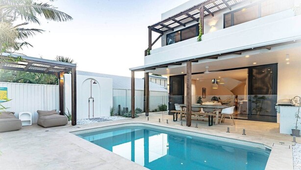 Una casa moderna con piscina, mobiliario exterior y un porche cubierto.