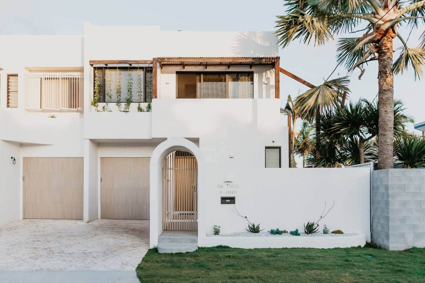 Une maison moderne à deux étages, avec une façade blanche, un patio couvert et un petit jardin.