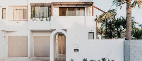 Una casa moderna de dos pisos con fachada blanca, un porche cubierto y un pequeño jardín.