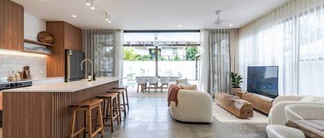 Una cocina moderna con una isla central, taburetes de bar, un comedor con mesa y sillas, un sofá y un televisor.
