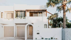 Una casa moderna de dos pisos con fachada blanca, un porche cubierto y un pequeño jardín.