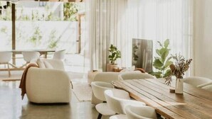 Un comedor moderno con una mesa de madera y sillas blancas, ventanas grandes y un ventilador de techo.