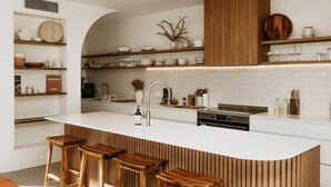 Una cocina moderna con una isla central, taburetes de bar, armarios de madera y salpicadero de azulejos blancos.