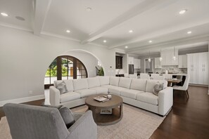 A spacious living room with a sectional sofa, a round coffee table, and a dining area with a kitchen in the background.