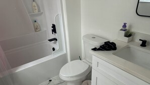 Un bagno con vasca, servizi igienici, lavandino e un piccolo ripiano con articoli da toilette.