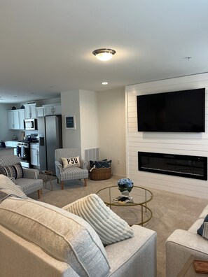 A modern living room with a flat-screen TV, striped armchairs, a sofa, and a kitchen in the background. - The Nittany House in Bellfonte (Bellefonte)