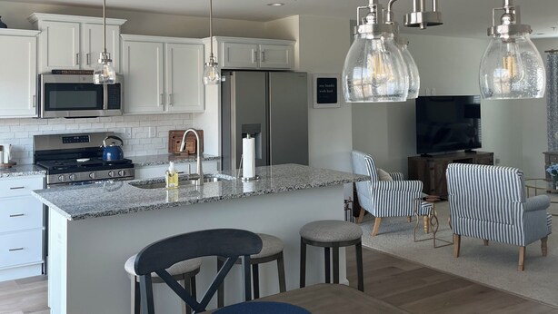 A modern kitchen with white cabinets, a stainless steel stove, and a dining area with a wooden table and chairs. - The Nittany House in Bellfonte (Bellefonte)