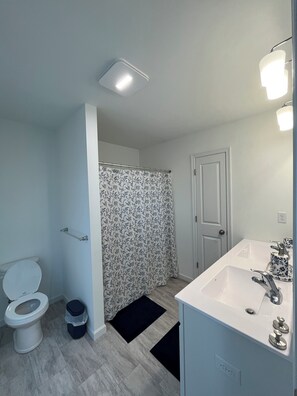 Une salle de bain équipée de toilettes, d’un rideau de douche, d’un lavabo et d’un luminaire.