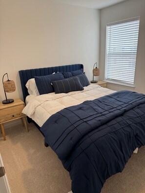 A bedroom with a bed, two bedside tables, a window with blinds, and a wall-mounted lamp. - The Nittany House in Bellfonte (Bellefonte)