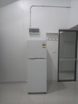 A white refrigerator with a Samsung Energy Star sticker, a wall-mounted electrical box, and a door with a glass panel.