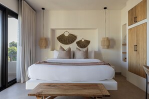 Ein modernes Schlafzimmer mit einem großen Bett, zwei Wandventilatoren, einem Holztisch und Blick auf Grünfläche.