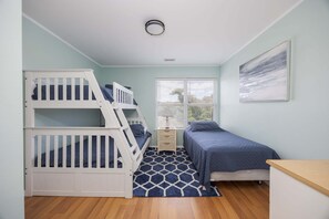 A room with bunk beds, a small bedside table, a lamp, a bed with a blue bedspread, and a window with blinds. - 1501 - Carolina Breeze, Top-Floor 2BR Monteray Pines: Screened Balcony (Corolla)