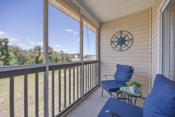 A covered porch with a view of the outdoors, a compass decoration, and blue seating. - 1501 - Carolina Breeze, Top-Floor 2BR Monteray Pines: Screened Balcony (Corolla)