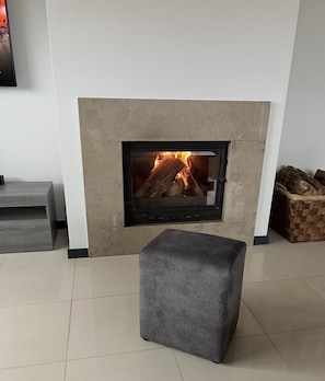 Ein modernes Wohnzimmer mit Kamin, grauer Ottoman und Fliesenboden.