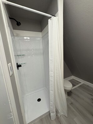 A shower with a white door, a glass shower door, and a white shower curtain.