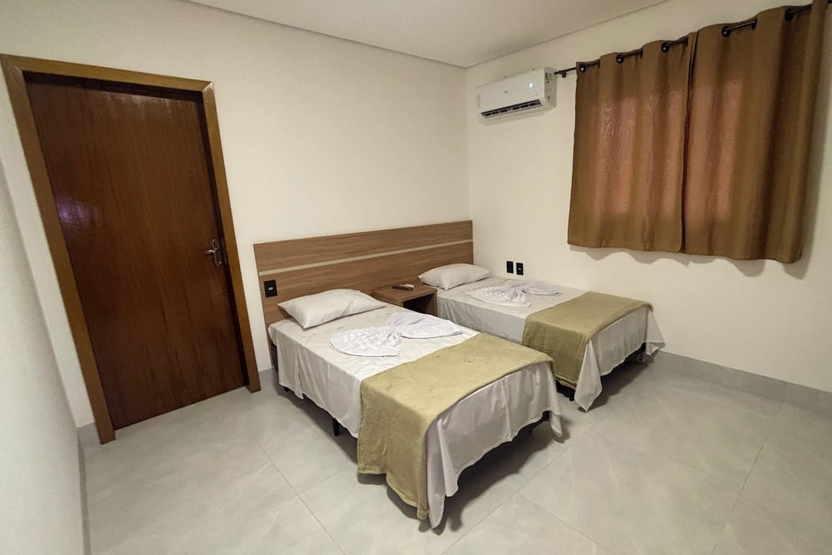 A hotel room with two beds, a wooden door, an air conditioning unit, and a curtain.