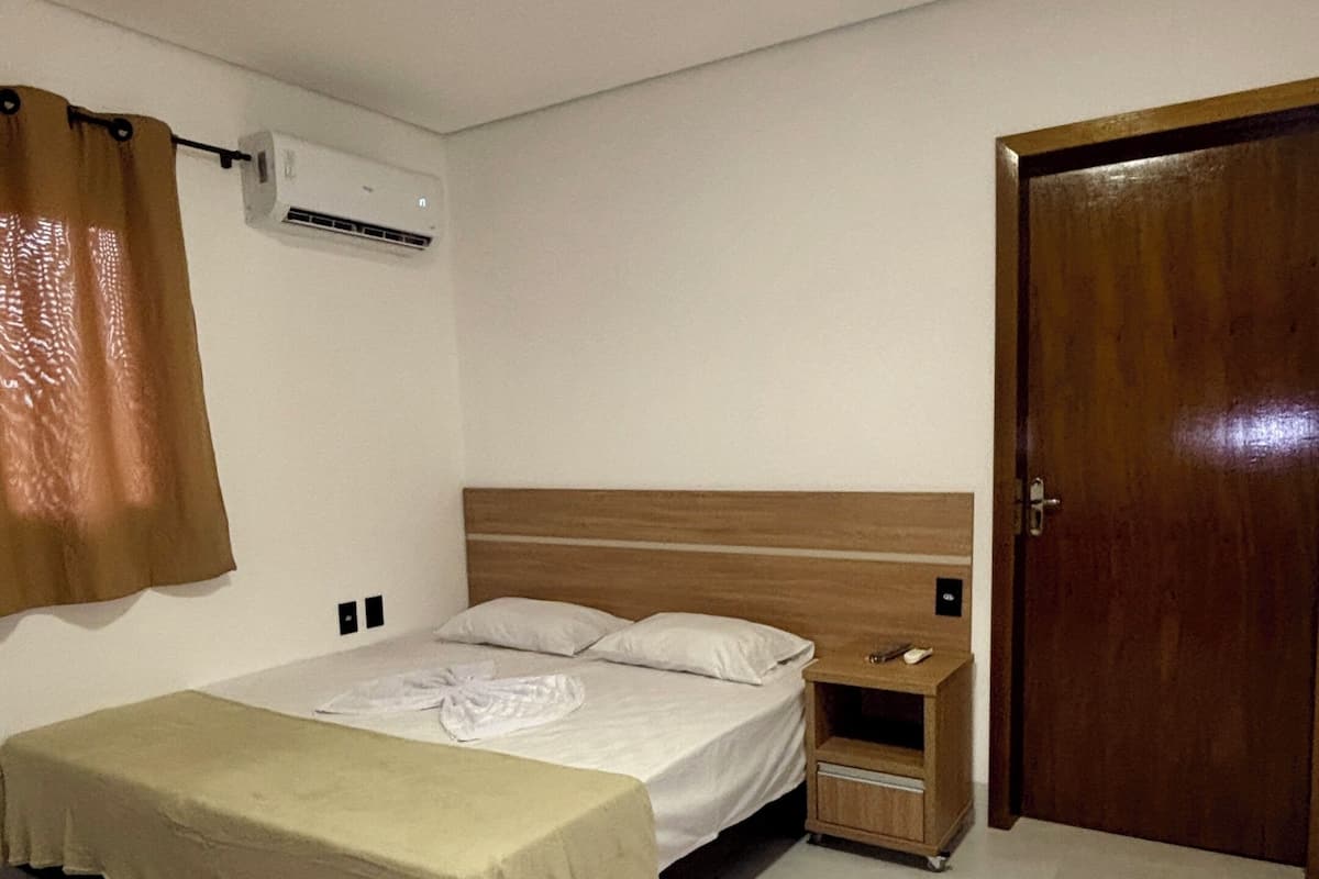 A bedroom with a bed, a nightstand, a wooden door, and an air conditioning unit on the wall.