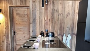 A modern kitchen with a wooden wall, a long countertop, and overhead lighting. - Discover this superb 3.5-room premium apartment, completely renovated with quality materials, combin (Thyon-Les Collons)
