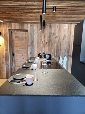 A modern kitchen with a wooden wall, a long countertop, and overhead lighting. - Discover this superb 3.5-room premium apartment, completely renovated with quality materials, combin (Thyon-Les Collons)