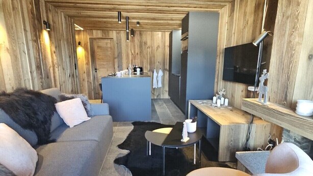 A modern interior with a sofa, a round chair, a small table, a TV, and a kitchen area. - Discover this superb 3.5-room premium apartment, completely renovated with quality materials, combin (Thyon-Les Collons)