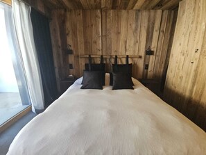 A wooden room with a bed, a window with curtains, and a wooden headboard. - Discover this superb 3.5-room premium apartment, completely renovated with quality materials, combin (Thyon-Les Collons)