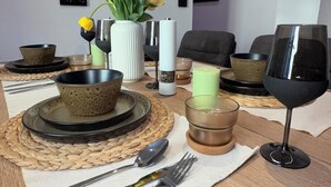 Une table à manger avec des assiettes, des bols, des couverts, un vase de fleurs, des bougies et un verre à vin.