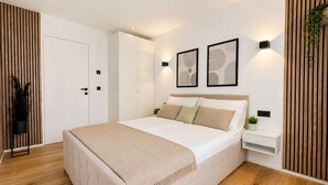 Une chambre moderne avec un grand lit, une armoire, une table de chevet et des luminaires fixés au mur.