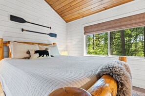 A bedroom with a large bed, wooden headboard, two paddles on the wall, and a window with a view of trees. - New Listing! Family Friendly Hot Tub Cabin+Fire Pit+Dogs Friendly+Close to BR! (Blue Ridge)