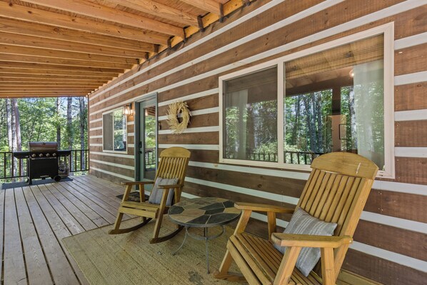 Een houten vakantiehuis met een veranda, schommelstoelen, een tafel en een barbecue.