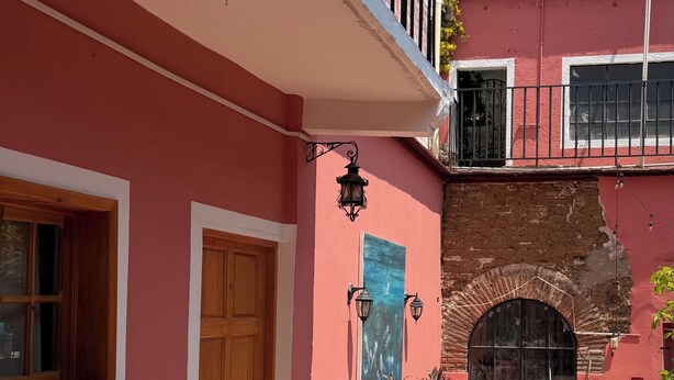 A red building with a wooden door, potted plants, and a tiled pathway. - A hotel in a café (Oaxaca de Juárez)