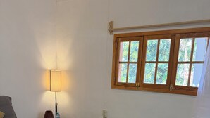 A bedroom with a bed, a nightstand, a lamp, a window, and a view of greenery outside. - A hotel in a café (Oaxaca de Juárez)